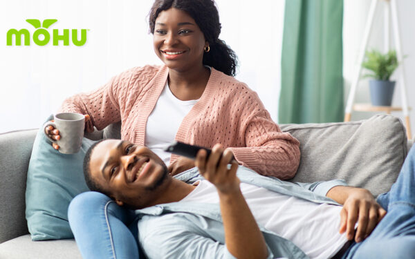 Couple laying on the couch watching Television, flipping through channels with remote in hand. Mohu logo.