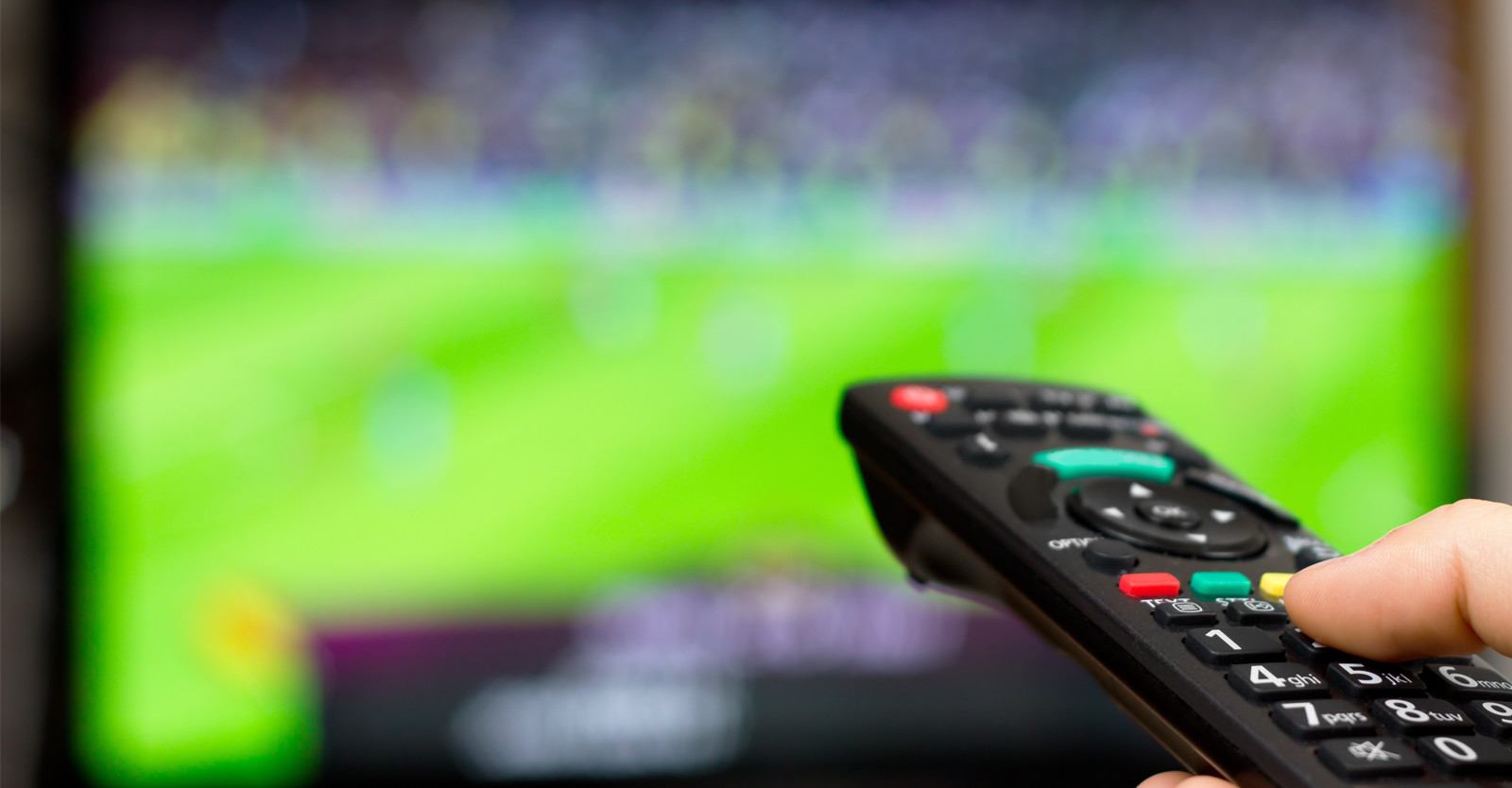Man using the TV remote with sports on in the background